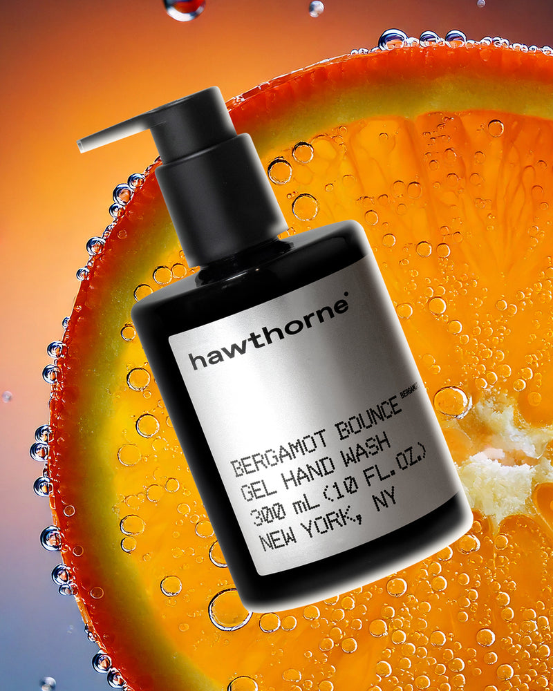 A black pump bottle of Hawthorne Bergamot Bounce gel hand wash is shown in front of a close-up slice of orange with water droplets on it.