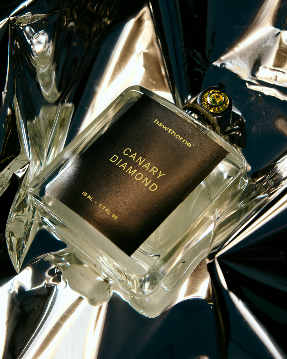 A bottle of Hawthorne Canary Diamond fragrance rests on reflective metallic material.