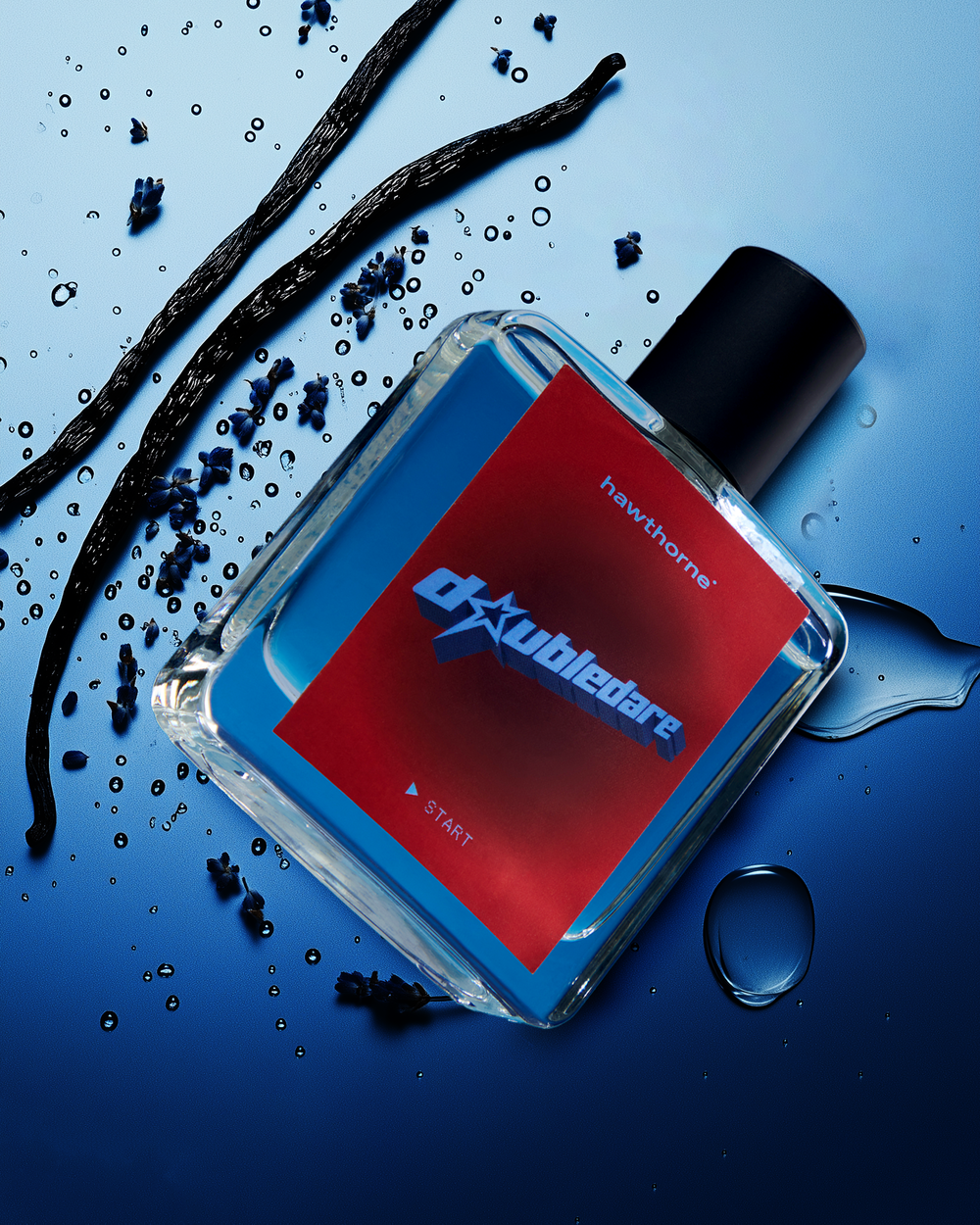 A rectangular perfume bottle labeled double dare on a red label lies on a blue surface, surrounded by black sticks and scattered blue crystals and water droplets.